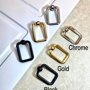 May include: A collection of rectangular metal hardware in black, gold, and chrome finishes. Each piece features a rounded top and a rectangular frame. The word "Chrome", "Gold", and "Black" are written on the image.