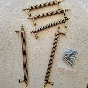 May include: Set of antique brass cabinet pulls with a ribbed design. The pulls have decorative end pieces and are shown with a small bag of screws. The pulls are approximately 8 inches long.