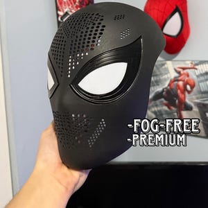 May include: A matte black full-face mask featuring a perforated texture across the forehead and chin areas, with large white eye lenses outlined in black. The text -FOG-FREE -PREMIUM is printed in white on the lower right side of the mask.