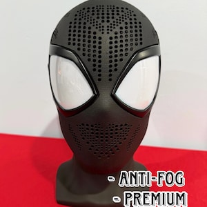 May include: A black full-head mask featuring a perforated texture across the forehead and mouth area, with large white mesh eye lenses. The mask includes text that reads ANTI-FOG and PREMIUM. The design covers the entire head and neck area.