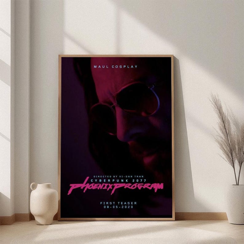 May include: A framed poster with a dark, futuristic theme. The poster features a close-up of a person's face with sunglasses, bathed in red and purple light. Text includes "MAUL COSPLAY" and "CYBERPUNK 2077 PHOENIX PROGRAM".