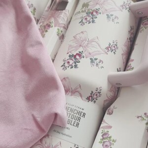 May include: A white Stanley Quencher H2.0 FlowState tumbler with a pink floral and ribbon pattern, featuring a matching pink handle and straw, packaged in a decorative box with a pink fabric item and text reading Stanley, Quencher, and 1.18 L.