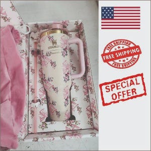 May include: A cream-colored Stanley tumbler with a floral and bow pattern, featuring a matching pink handle and straw, presented in a decorative box with a pink fabric item. The tumbler has the Stanley logo and the text SHACKFAN printed on the front.