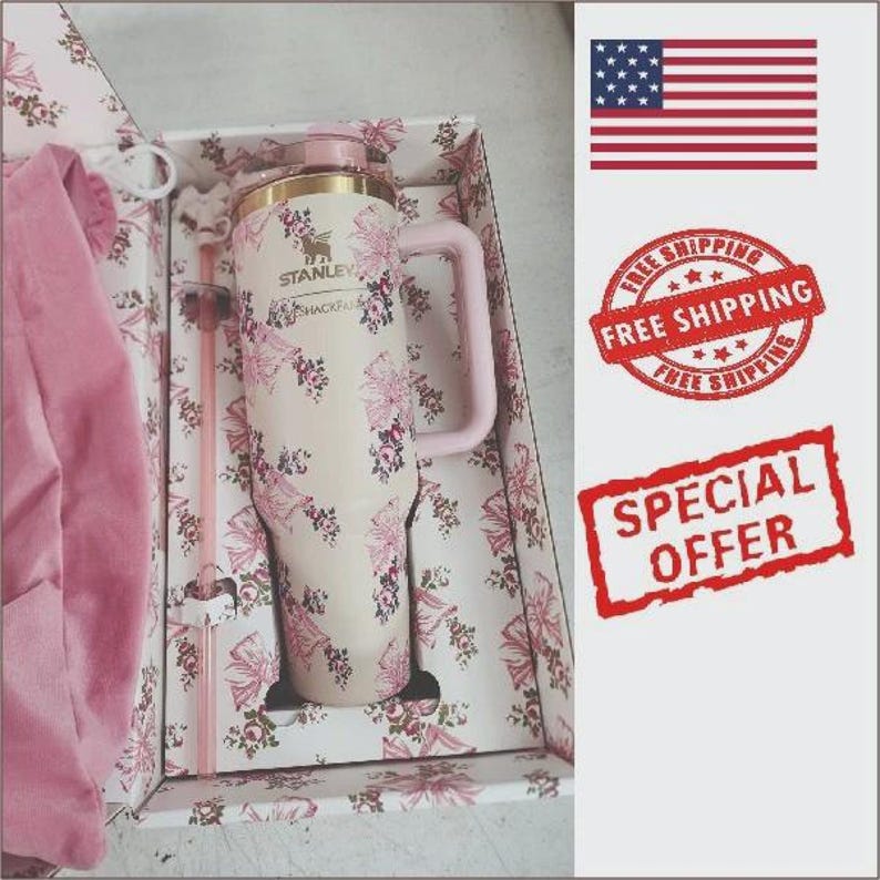May include: A cream-colored Stanley tumbler with a floral and bow pattern, featuring a matching pink handle and straw, presented in a decorative box with a pink fabric item. The tumbler has the Stanley logo and the text SHACKFAN printed on the front.