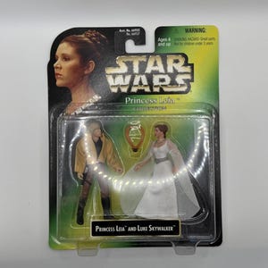 Op de afbeelding: Star Wars Princess Leia en Luke Skywalker actiefiguren in originele verpakking. De verpakking toont een afbeelding van Princess Leia, het Star Wars logo en een waarschuwing. De figuren zitten in een doorzichtige plastic verpakking.