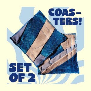 Op de afbeelding: Een set van twee vierkante onderzetters met een geometrisch patchworkontwerp van metallic blauwe, beige en grijze stof. De onderzetters hebben zichtbare stiksels en gerafelde randen. De tekst "COASTERS! SET OF 2" is in het blauw afgedrukt.