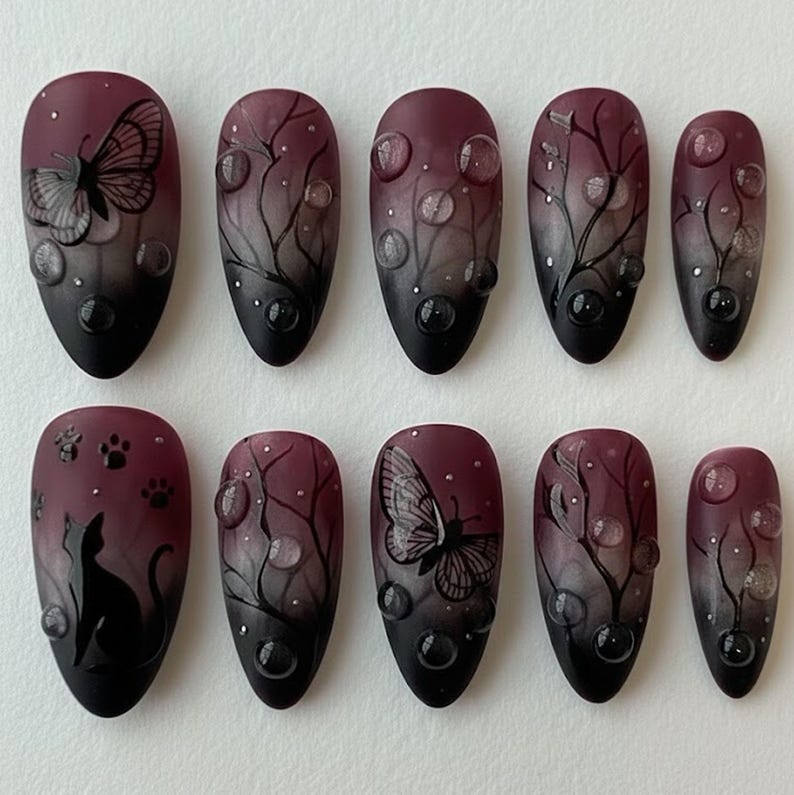 May include: Set of ten oval-shaped, burgundy and black press-on nails. Designs include butterflies, cat silhouettes, paw prints, and tree branch patterns with water droplet accents. The nails have a matte finish.