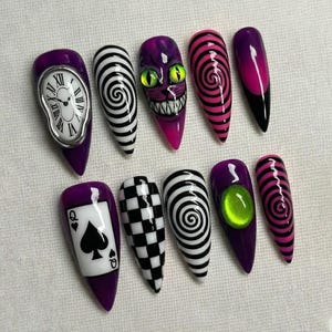 May include: A set of ten long, pointed artificial nails with various designs. The designs include a melting clock, a spiral, a checkerboard, a Cheshire Cat face, a playing card, and a green gem. The nails are primarily purple, black, white, and pink.