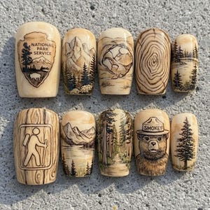 May include: A collection of ten wooden nesting dolls, each hand-painted with nature-themed designs. The dolls feature images of mountains, forests, Smokey Bear, and the National Park Service logo. The dolls are beige with brown and green accents.