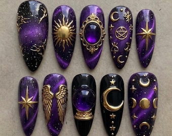 Puede incluir: Un juego de diez uñas postizas en forma de almendra con una base de color púrpura y negro inspirada en la galaxia, con dijes celestiales dorados que incluyen soles, lunas, estrellas, alas, una gema púrpura central y una bola de cristal.