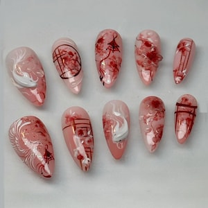 May include: A set of ten almond-shaped artificial nails. Each nail features a pink base with intricate designs in red and white. The designs include koi fish, architectural elements, and abstract patterns.