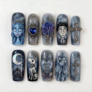 Könnte beinhalten: Ein Set aus zehn künstlichen Fingernägeln in Grau- und Blautönen mit detaillierten 3D-Verzierungen. Die Motive zeigen eine weibliche Figur, einen blauen Herzrahmen, violette Rosen, eine männliche Figur, silberne Kreuze, einen Mond und ein Kleid.