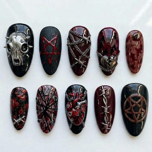 Könnte beinhalten: Ein Set aus zehn künstlichen Nägeln mit einem dunklen, gotischen Thema. Designs umfassen einen Schädel, Pentagramme, Stacheldraht, Ketten und ein zerbrochenes Herz, alles in Schwarz-, Rot- und Silbertönen. Die Nägel haben ein glänzendes Finish.