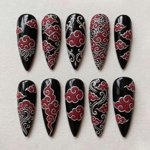 May include: A set of ten black, glossy press-on nails. Each nail is decorated with a design of red clouds with silver detailing. The cloud patterns vary across the nails. The nails are almond-shaped, offering a unique look.