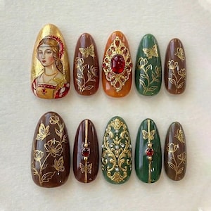 May include: A collection of ten oval press-on nails with detailed designs. The nails display gold, brown, orange, and green hues. Some nails feature portraits, butterflies, floral patterns, and ornate jewel accents, offering a regal aesthetic.
