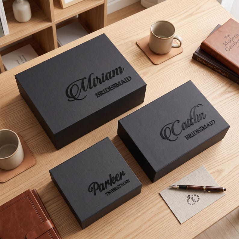 May include: Three rectangular black gift boxes with lids, each featuring custom black embossed text. The largest box is labeled Miriam BRIDESMAID, the medium box says Caitlin BRIDESMAID, and the smallest box is marked Parker THEBESTMAN.