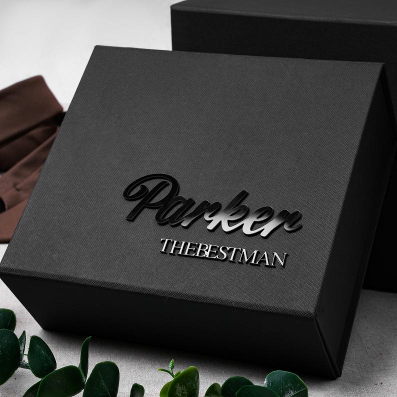 May include: A square black gift box with a matte finish featuring the name Parker in a large, glossy, cursive script font, followed by the text THEBESTMAN in a smaller, clean, sans-serif capital letter font centered on the lid.