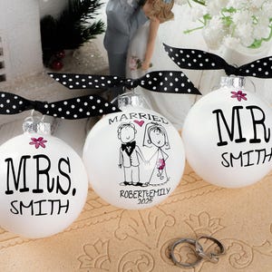 May include: Three white Christmas ornaments with black text and polka dot ribbons. One ornament says "MRS. SMITH", another says "MARRIED" with a couple illustration, and the third says "MR. SMITH".