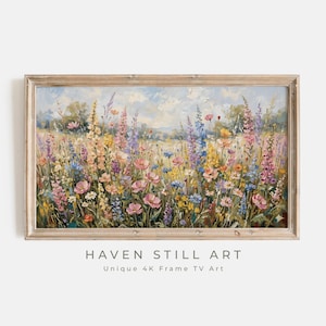 May include: A framed painting of a vibrant wildflower meadow. The artwork features a variety of colorful flowers in shades of pink, purple, yellow, and blue, set against a soft, cloudy sky. The frame is a light, natural wood. Text at the bottom reads "HAVEN STILL ART".
