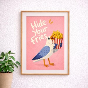 May include: A framed art print featuring a cartoon seagull holding a container of french fries. The seagull is white with blue wings and orange legs. The background is pink with the words "Hide Your Fries" in white.