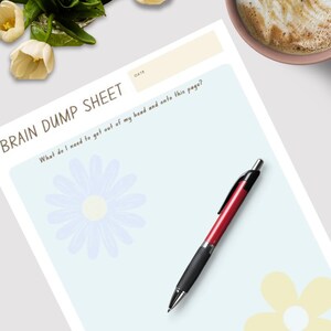 Op de afbeelding: Een Brain Dump Sheet met de tekst "What do I need to get out of my head and onto this page?" en een rood-zwarte pen. Het vel heeft een lichtblauwe achtergrond met bloemillustraties. Een kopje koffie en een boeket witte tulpen staan ook op de foto.