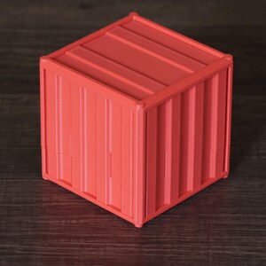 May include: A small, cube-shaped storage container in a vibrant coral-red color. The exterior features a corrugated, ribbed texture that mimics the appearance of a standard industrial shipping container, complete with vertical and horizontal lines.