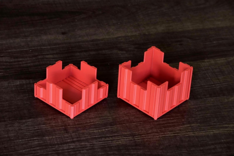 May include: Two red, square-shaped containers with crenelated, castle-like walls. The containers feature vertical ribbed detailing on the exterior sides and a flat base. One container is shorter than the other, and both have open tops.