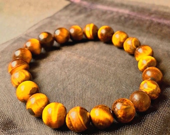 May include: A circular bracelet composed of polished, spherical tiger's eye beads. The beads feature a natural chatoyant pattern with alternating bands of golden-yellow and dark brown tones, strung together on a flexible cord to form a continuous loop.