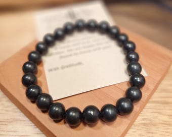 May include: A circular stretch bracelet composed of smooth, round, matte black beads. The bracelet is arranged in a ring shape, showcasing the uniform size and dark, non-reflective surface of each individual bead strung together on an elastic cord.