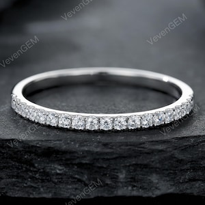 Peut inclure: Une fine bague en métal argenté ornée d'une rangée continue de petites pierres rondes et transparentes à facettes sur la moitié avant. Le métal présente une finition polie et réfléchissante, avec des pierres serties en griffes partagées.
