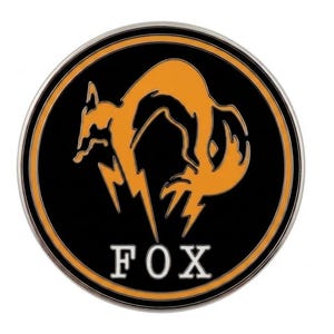 May include: A circular metal pin featuring a black background with an orange stylized fox silhouette and a lightning bolt design. The word FOX is printed in white capital letters at the bottom, all enclosed within a thin silver metallic border.