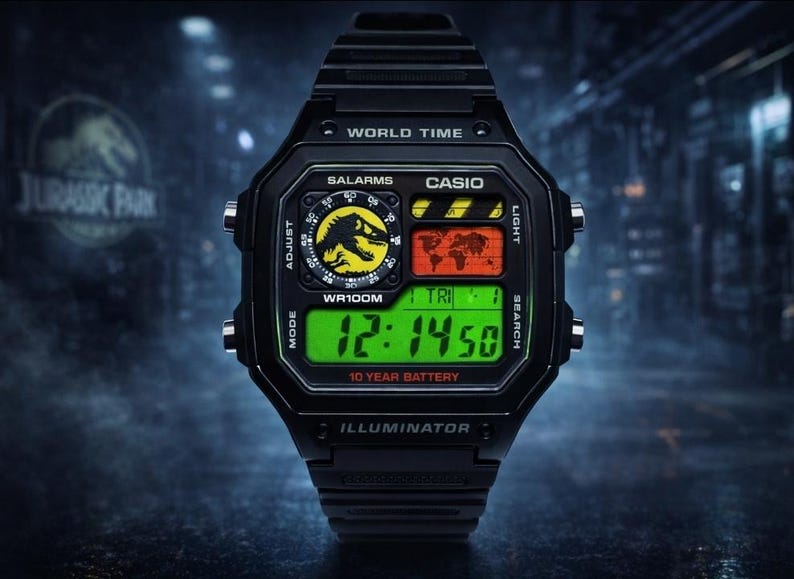 May include: A black Casio digital watch featuring a Jurassic Park logo on the circular dial, a world map display, and a bright green digital time readout. The watch face includes text reading WORLD TIME, SALARMS, WR100M, and 10 YEAR BATTERY.