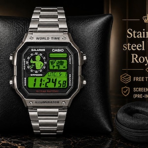 May include: A silver-tone stainless steel digital watch with a green backlit display featuring a Fallout Vault Boy graphic, world time, and 10-year battery text. The watch includes a metal link band and is displayed with a small black travel case.