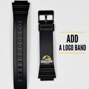 May include: Two black watch straps made of flexible material. One strap features a buckle and a yellow and black Jurassic Park logo graphic. The text ADD A LOGO BAND is printed in black next to the straps with yellow horizontal lines above and below.