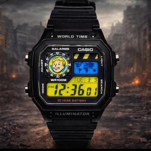 Op de afbeelding: Zwarte Casio digitale horloge met een Fallout-thema. De wijzerplaat toont de tijd, datum en een Vault Boy-afbeelding. Functies zijn wereldtijd, alarmen en een batterij van 10 jaar. Het horloge heeft een zwarte band en een geel digitaal display.