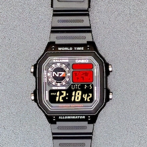 Puede incluir: Reloj digital Casio negro con esfera rectangular. El reloj muestra la hora, la fecha y las funciones de hora mundial. El reloj tiene una correa negra y una pantalla digital con el texto "WORLD TIME" e "ILLUMINATOR".