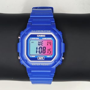 Puede incluir: Un reloj digital Casio azul con una esfera rectangular que muestra la fecha y la hora. El reloj tiene una correa azul y el texto "ILLUMINATOR", "CASIO" y "WATER RESIST" son visibles.