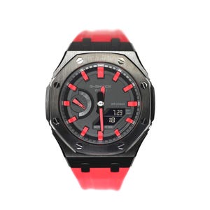 May include: A G-Shock Casio watch featuring a black octagonal bezel with exposed screws, a dark gray dial with bright red hour markers, and red hands. The watch includes a digital display showing 7.29 and 18, and a vibrant red silicone strap.
