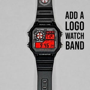 May include: Black digital watch with a red display showing the time. The watch band features the Umbrella Corporation logo. The text "ADD A LOGO WATCH BAND" is displayed next to the watch.