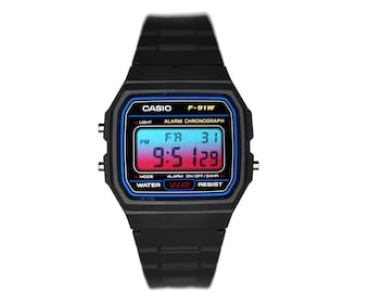 Puede incluir: Un reloj de pulsera digital negro con una esfera rectangular que presenta el texto CASIO F-91W. La pantalla muestra un fondo degradado de azul a rojo, indicando la hora 9:51 y la fecha FR 31. Incluye una correa de resina de color negro.