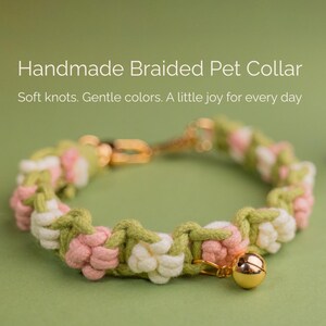 May include: A handmade braided pet collar with a floral design in pink, white, and green. The collar has a gold-coloured bell charm. The image text reads "Handmade Braided Pet Collar". The collar is designed for pets.