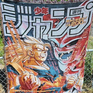 Puede incluir: Una manta tejida con una vibrante ilustración de personajes de la serie de anime Dragon Ball. El diseño incluye texto japonés y poses de acción dinámicas en tonos naranja, azul y rojo. La manta tiene un borde con flecos.