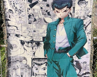 Può includere: Una coperta tessuta con un'illustrazione in stile manga di un personaggio in abito verde acqua, su uno sfondo di fumetti in bianco e nero. La coperta ha un bordo sfrangiato ed è esposta all'aperto.