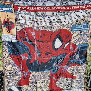 May include: A woven Spider-Man comic book cover blanket. The blanket features a large image of Spider-Man in his classic red and blue suit, with the title "Spider-Man" in large white letters. The blanket also includes comic book text and the words "Torment Part One of Five".