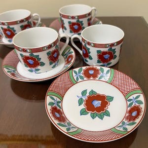 May include: A set of white porcelain teacups and saucers with a floral design. The cups and saucers feature a red and green floral pattern with blue accents. The set includes four cups and saucers and one plate.