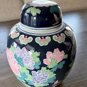 May include: A navy blue ceramic ginger jar with a matching lid. The jar is decorated with pink, purple, and green floral designs. The lid has a floral pattern and a white and blue band.