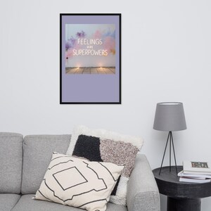 Puede incluir: Un cuadro decorativo enmarcado que muestra una imagen rectangular de una pared blanca con nubes de humo en tonos pastel rosa y morado. El texto "FEELINGS ARE SUPERPOWERS" aparece en letras mayúsculas blancas en el centro del humo, sobre un fondo morado claro.