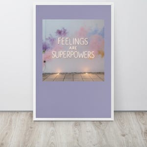 Puede incluir: Una lámina de arte mural enmarcada que presenta un letrero de neón blanco con el texto FEELINGS ARE SUPERPOWERS sobre un fondo de nubes de humo suaves en tonos violeta, rosa y amarillo. El marco es blanco con un borde violeta claro.