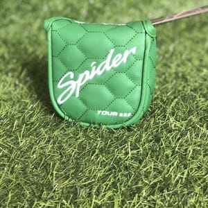Puede incluir: Una funda para la cabeza del putter de golf verde con la palabra "Spider" en escritura blanca. La funda tiene un patr&oacute;n acolchado y el texto "TOUR III" en la parte inferior. La funda descansa sobre un lecho de hierba verde.