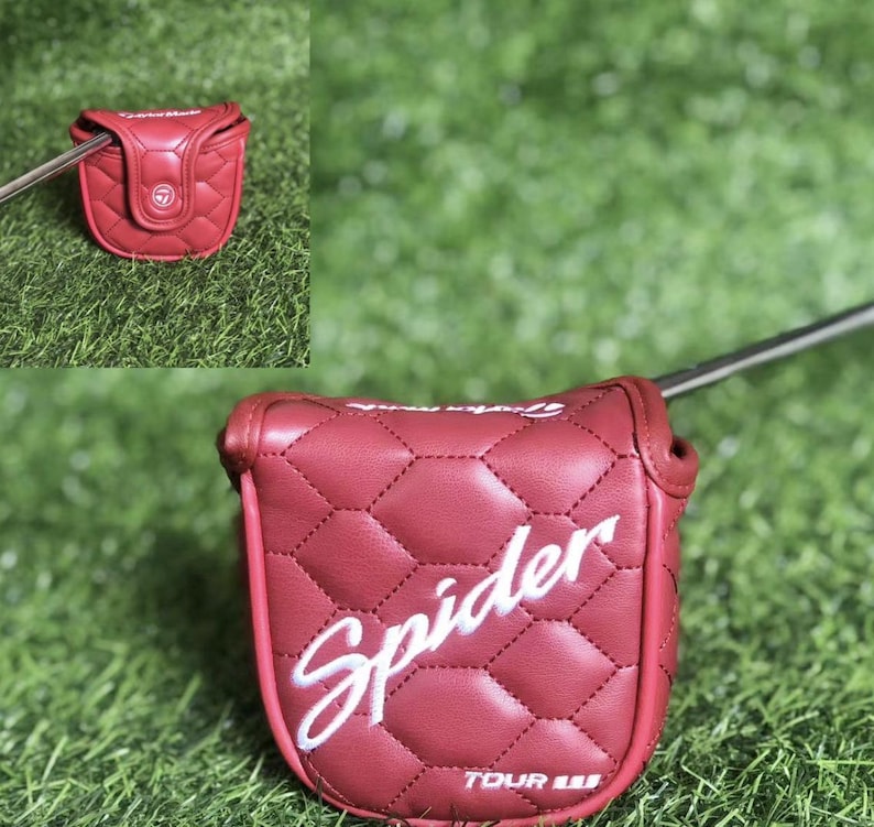 Puede incluir: Una funda de putter de golf acolchada roja con la palabra "Spider" en escritura blanca. La funda tiene un patr&oacute;n de diamantes y un cierre magn&eacute;tico. Sobre un fondo de hierba verde.